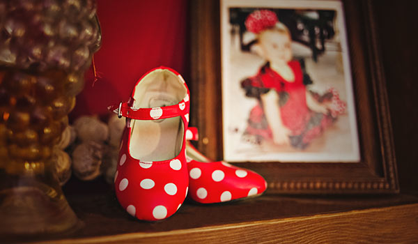 Zapatos de flamenca rojos de lunares junto al retrato de una niña vestida de flamenca